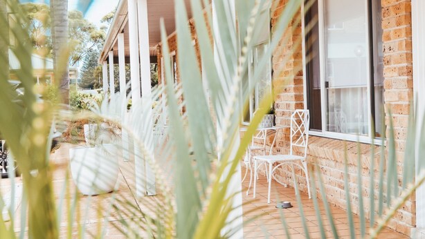 A brick house with a covered porch, white chairs, and a small table. - Harbourview House (Bermagui)