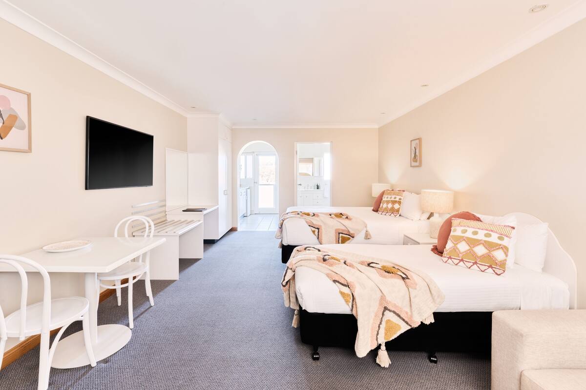 A hotel room with a bed, bedside table, lamp, and a desk with chairs.