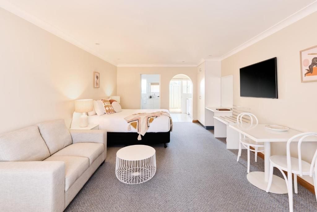 A modern hotel room with a bed, a sofa, a dining table, and a TV.