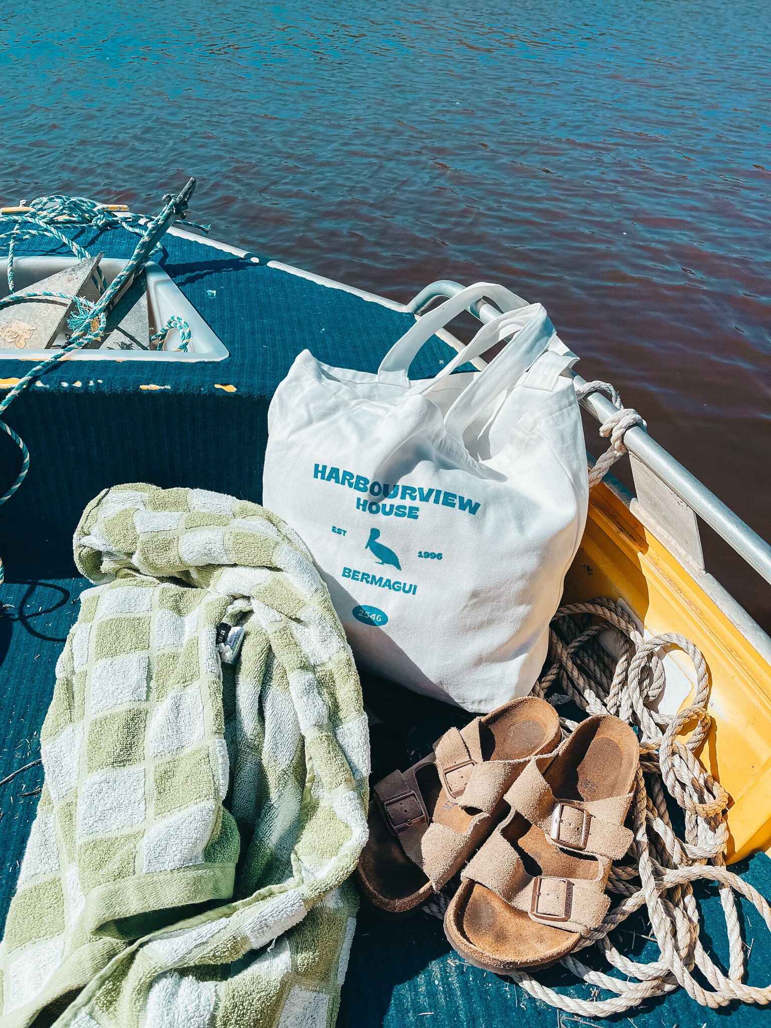 A boat with a white bag labeled "Harbourview House", a green towel, and sandals.