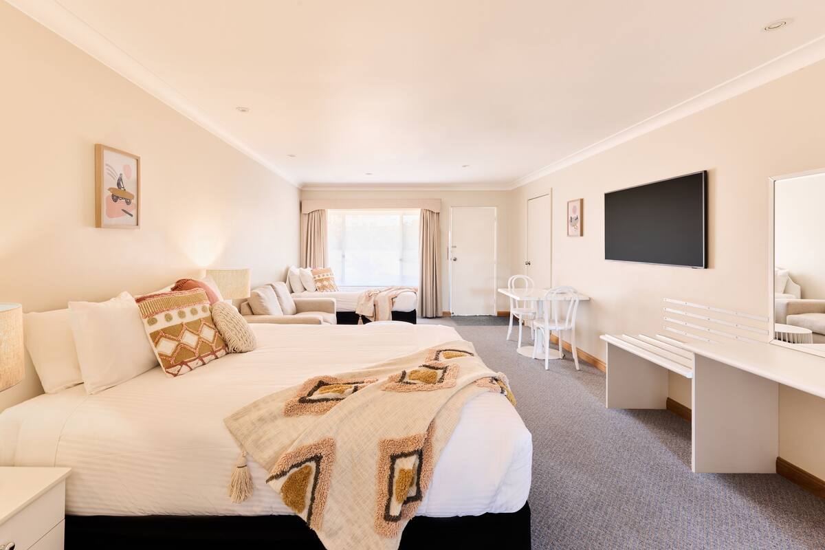 A hotel room with a large bed, a desk, a chair, a TV, and a window with curtains.