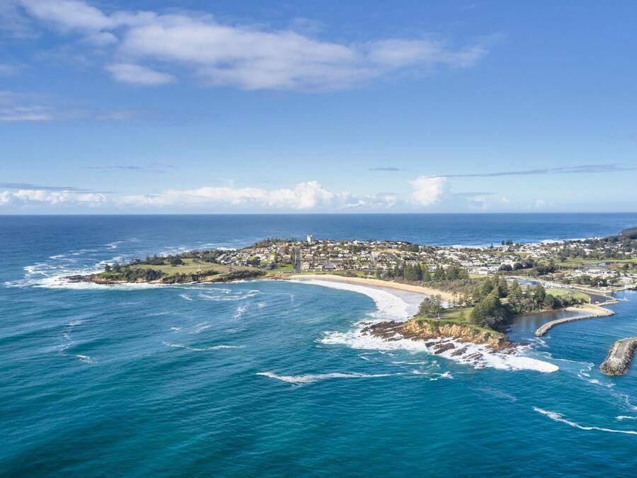 An aerial view of a coastal town with a beach, houses, and a clear blue sky.