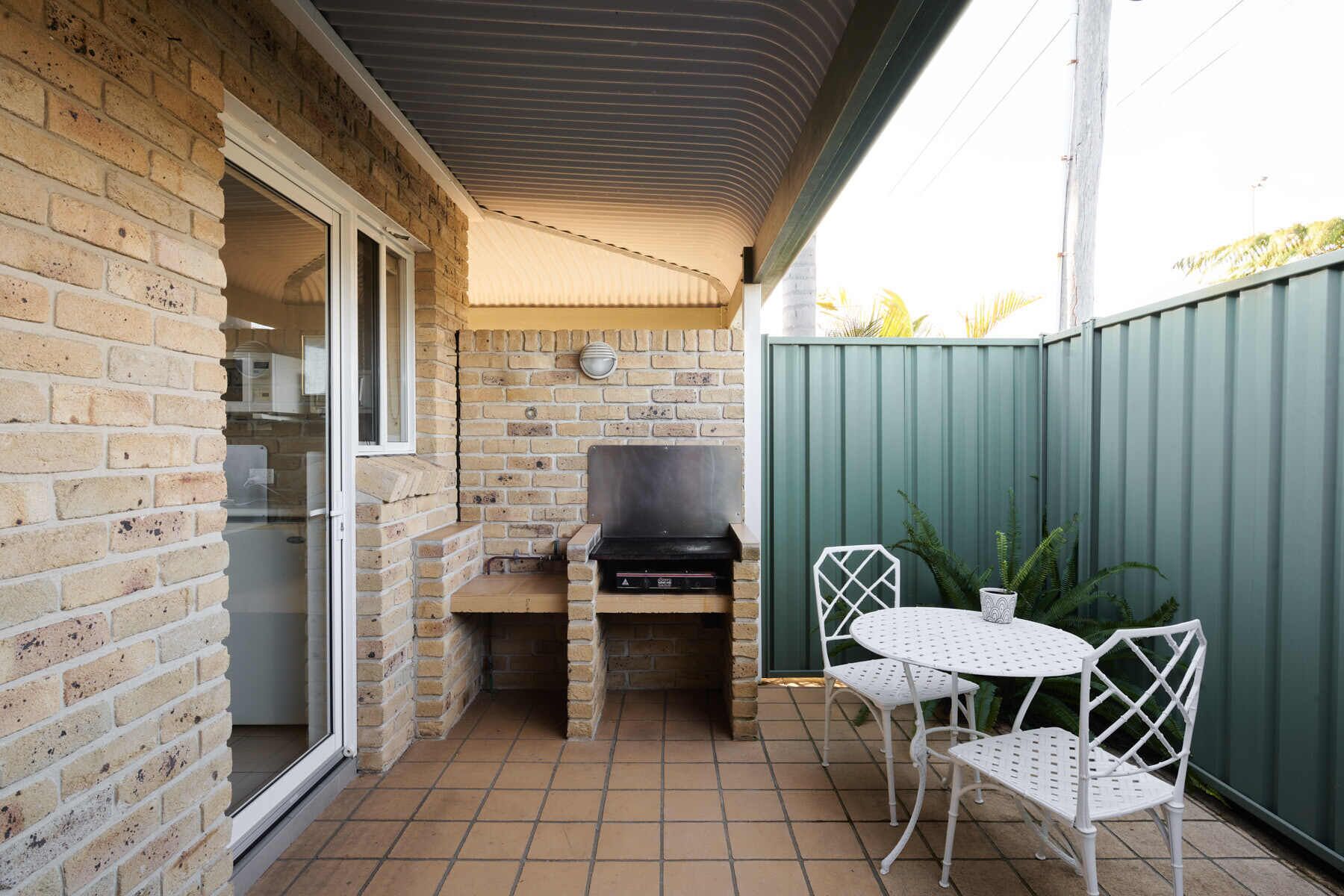A brick patio with a grill, a table, and chairs.