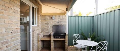 A brick patio with a grill, a table, and chairs.