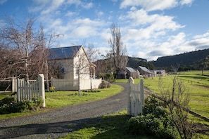 A rural property with a gravel driveway leading to a white gate, surrounded by trees and a clear sky. - Margate Cottage Boutique Bed & Breakfast (Margate)