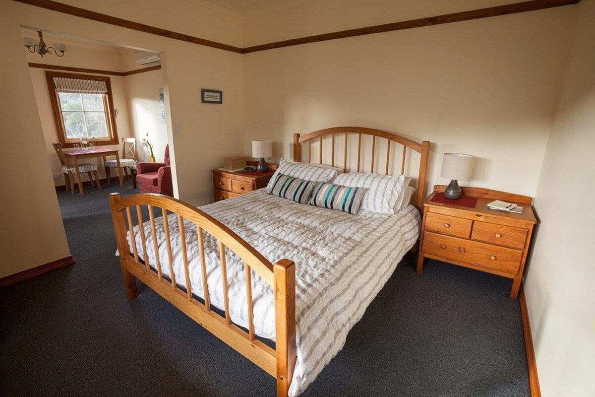A bedroom with a wooden bed, two bedside tables, a desk, and a chair.