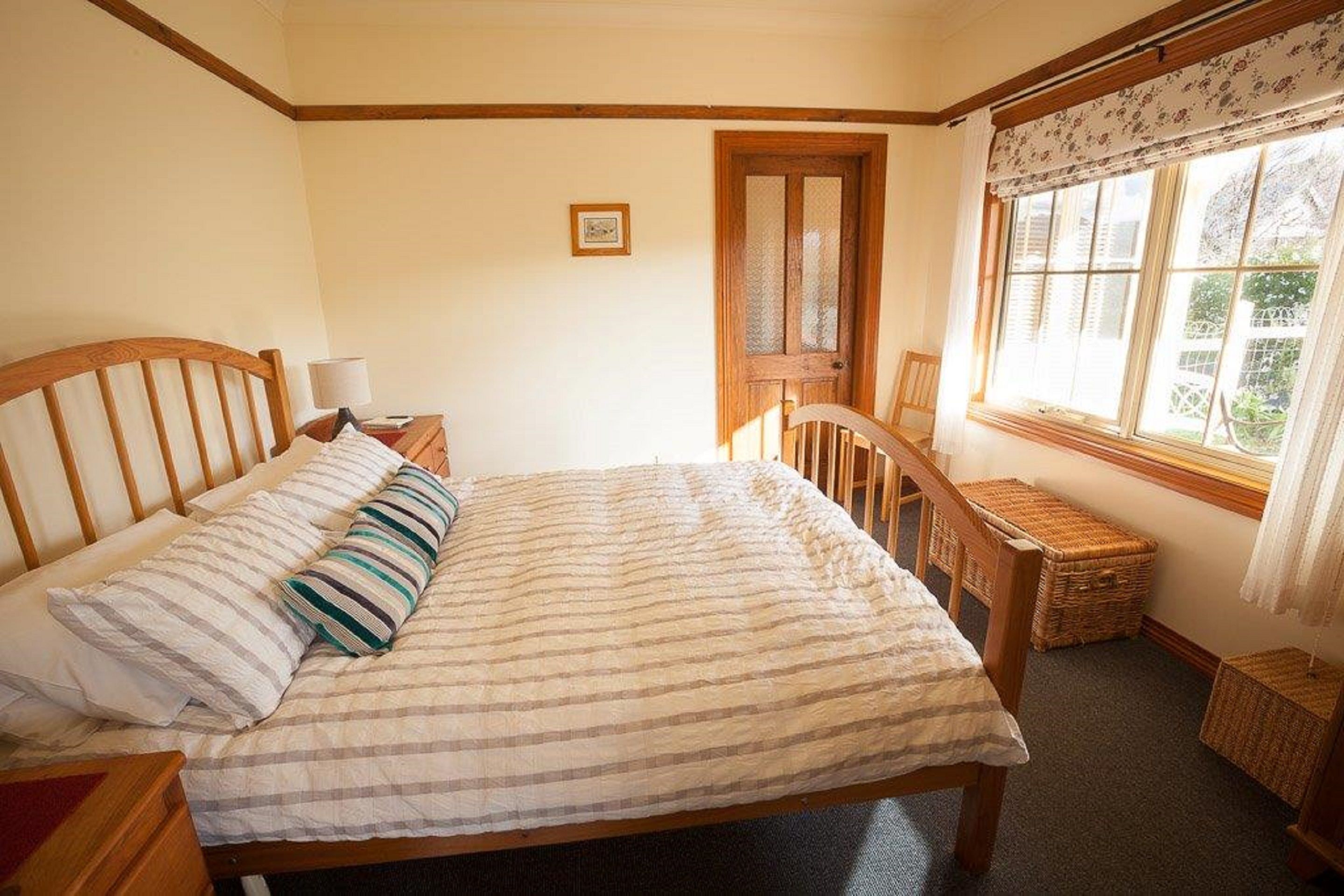Une chambre à coucher avec un lit en bois, une table de chevet, une chaise, une fenêtre avec des rideaux et une porte.