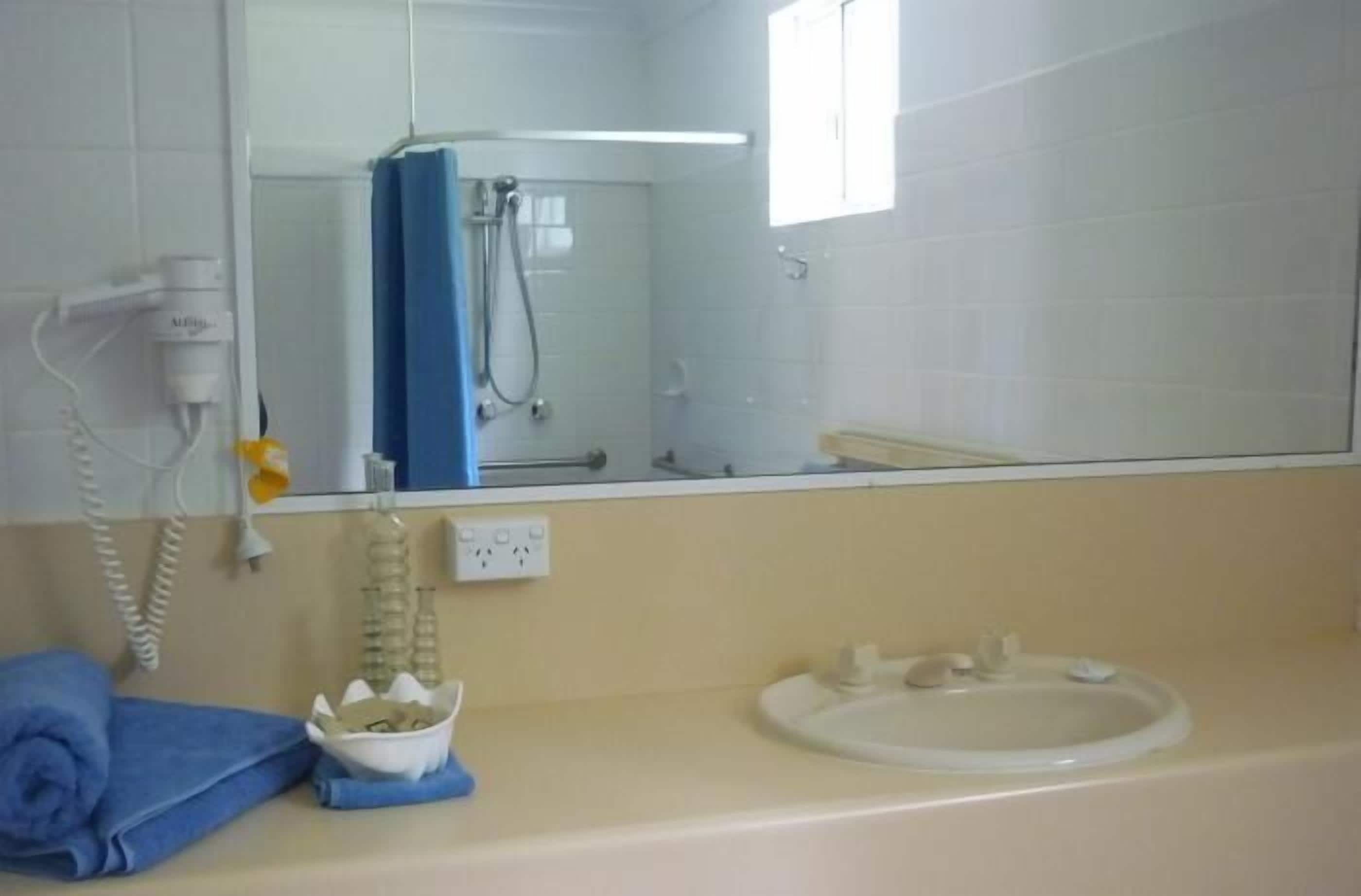 Ein Badezimmer mit Waschbecken, blauem Handtuch, Spiegel und Duschbereich.