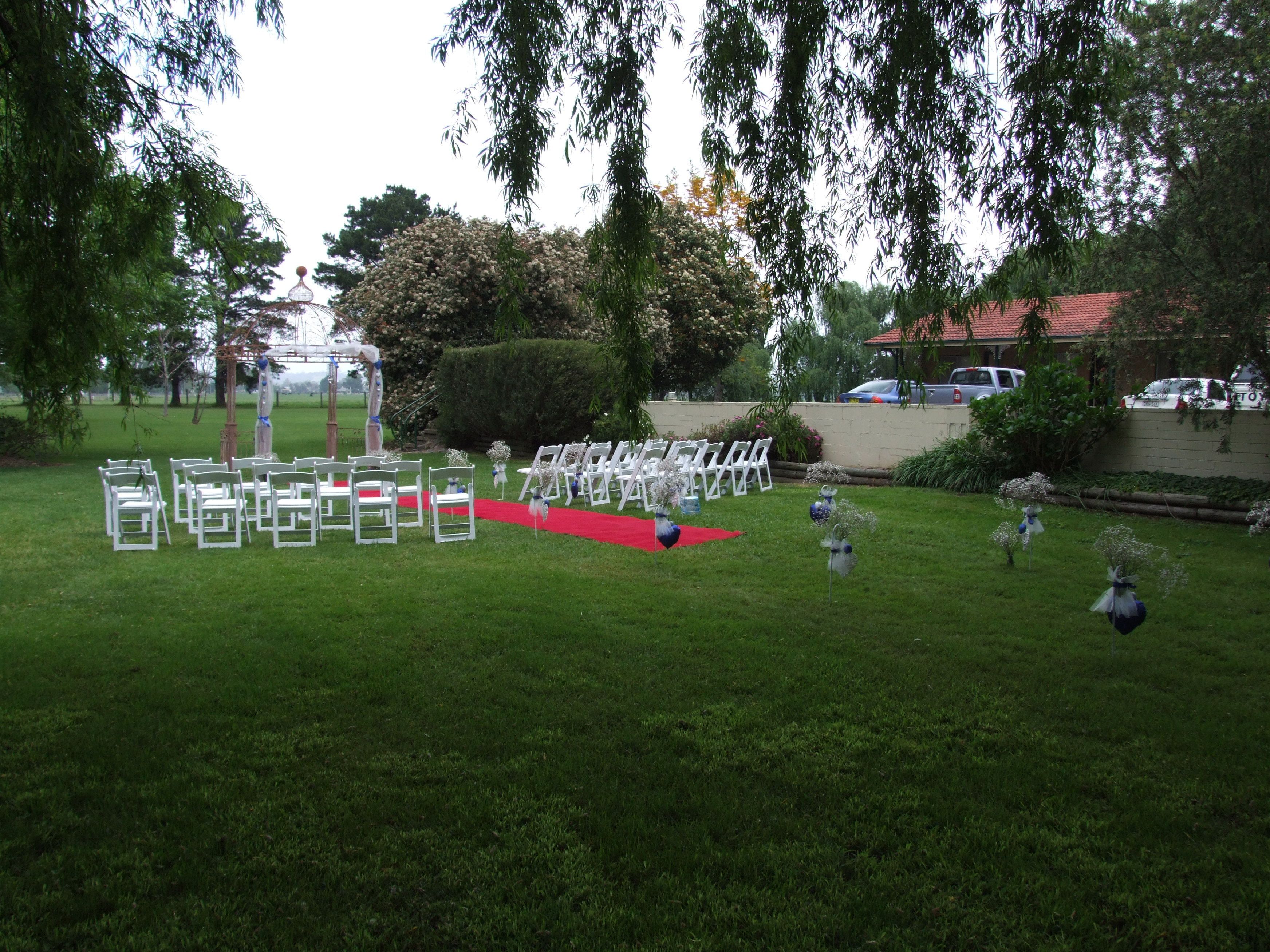 Een huwelijksdecoratie buiten, met witte stoelen en een rode loper.