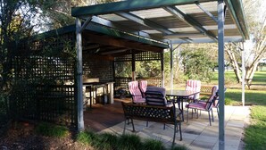 A covered patio area with a pergola, outdoor seating, and a grill. - Moruya Motel (Moruya)