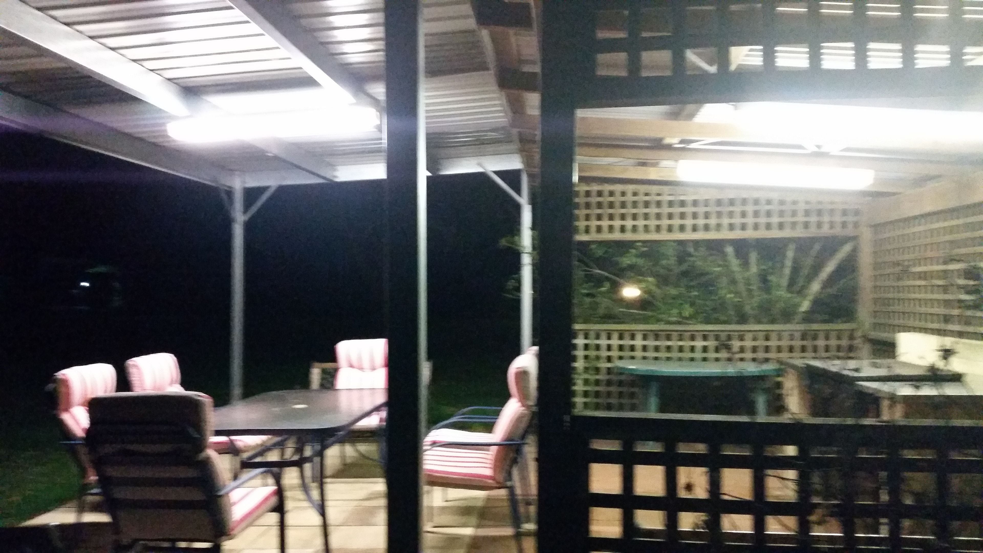 An outdoor patio area with a table and chairs, a small table with a lamp, and a view of a building with a lattice fence.