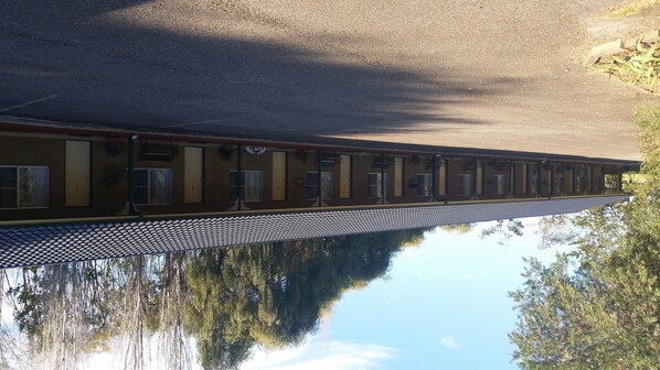 A long, single-story motel with a row of rooms featuring large windows and a tiled roof. - Moruya Motel (Moruya)