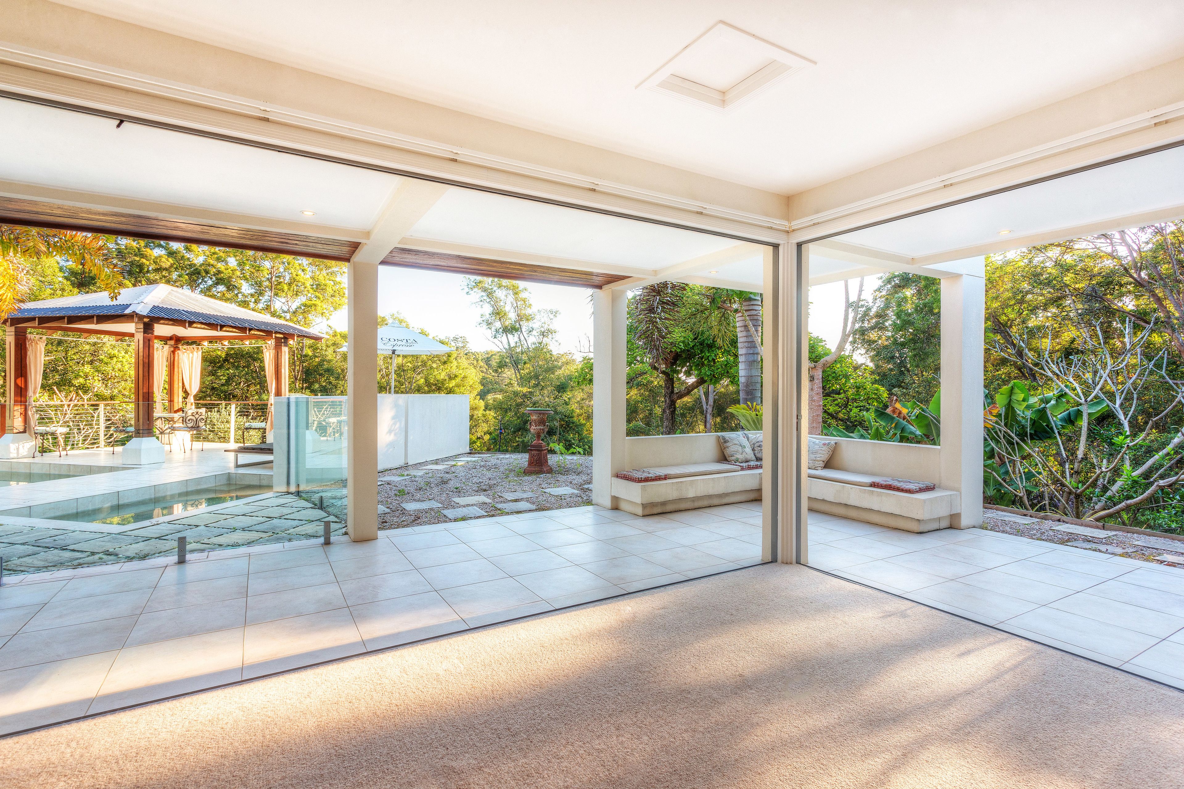 Un patio exterior moderno con cerramiento de vidrio, piscina y una zona de estar con cojines.