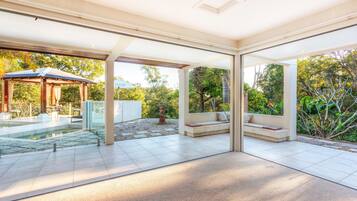 A modern outdoor patio with a glass enclosure, a pool, and a seating area with cushions.