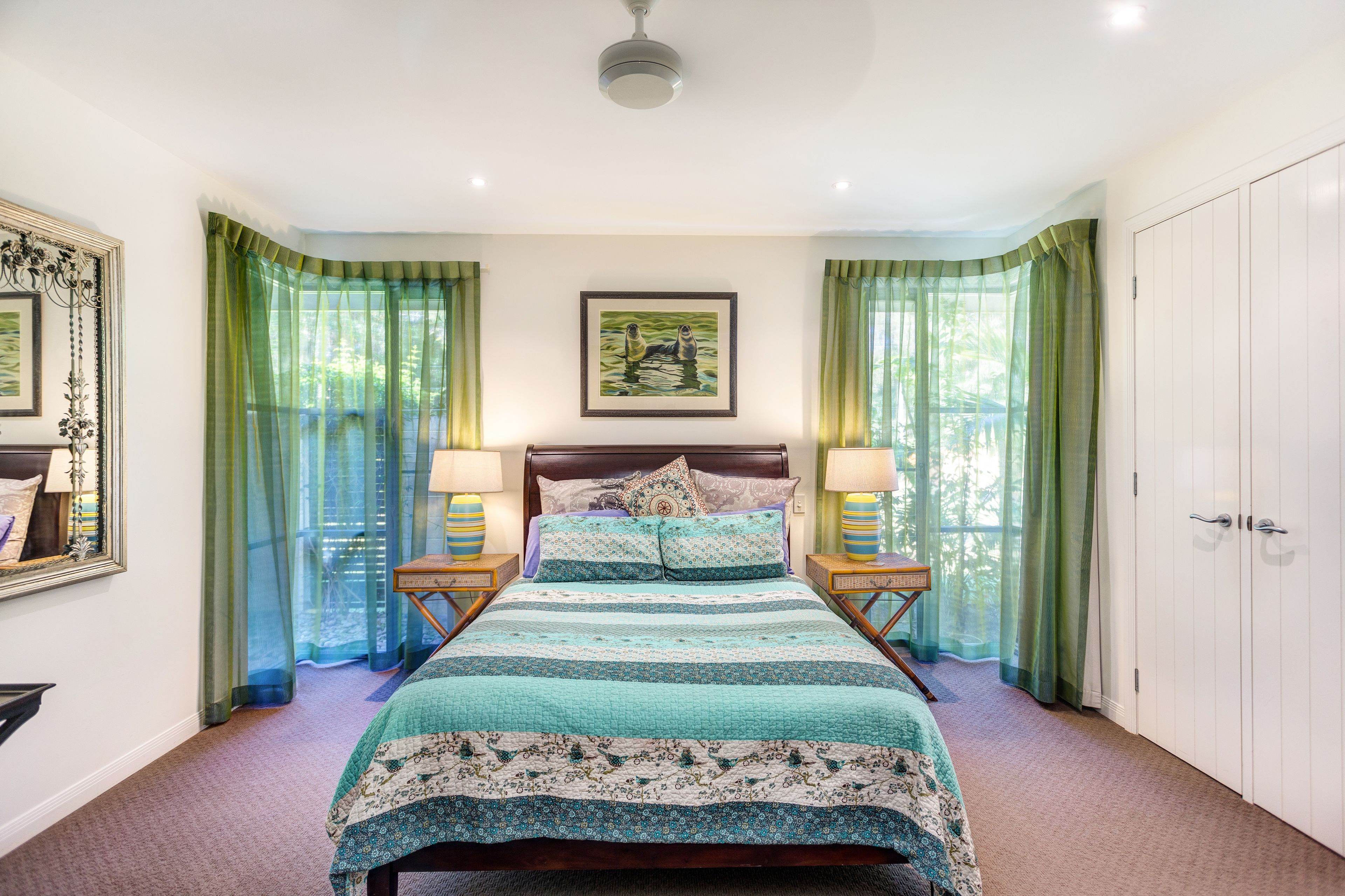 A bedroom with a bed, green curtains, a framed picture on the wall, and a nightstand with a lamp.