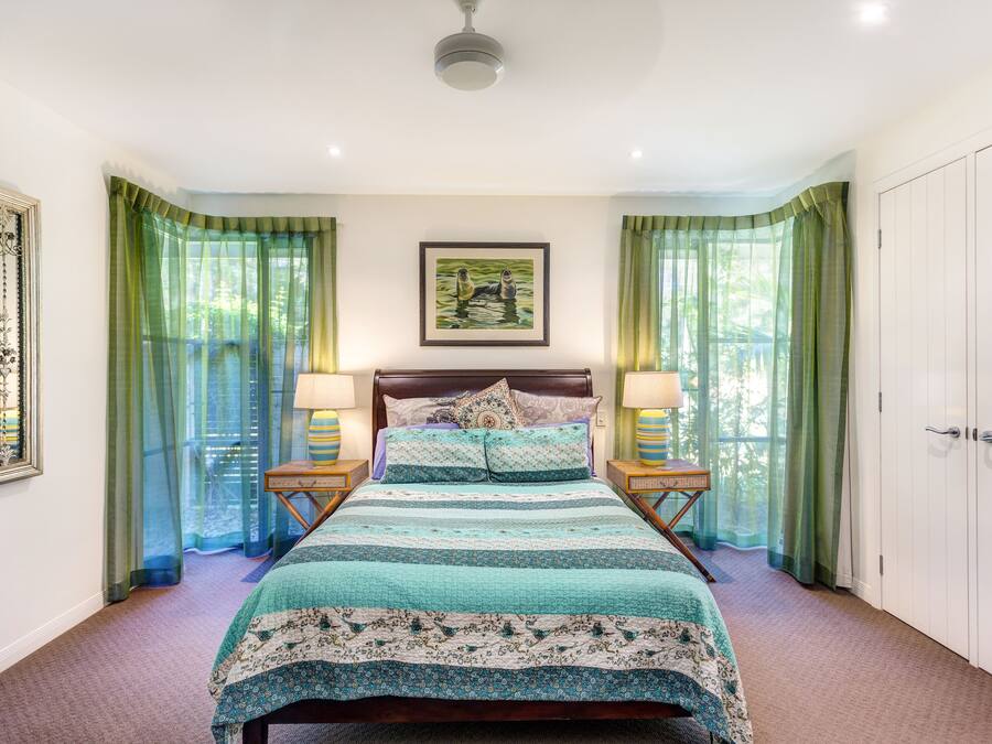 A bedroom with a bed, green curtains, a framed picture on the wall, and a nightstand with a lamp.