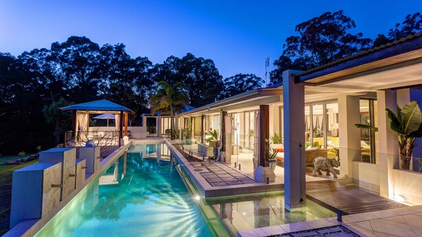 Una casa moderna con piscina, un porche cubierto y un gran ventanal que da a una sala de estar.