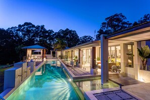 Una casa moderna con piscina, un porche cubierto y un gran ventanal que da a una sala de estar.