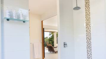 A modern bathroom with a shower, a glass shelf with toiletries, and a view of the outdoor seating area.