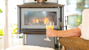Una persona sosteniendo un vaso de bebida en una habitación con chimenea y sofá.