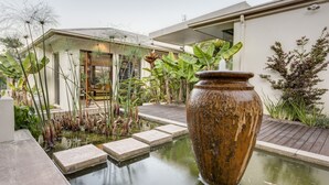Una casa moderna con un estanque en el jardín, un jarrón grande y diversas plantas.