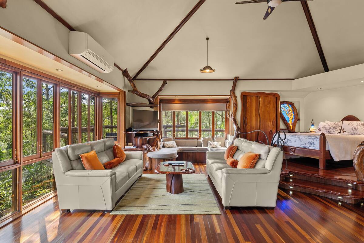 A spacious living area with large windows, a ceiling fan, and a cozy seating arrangement.
