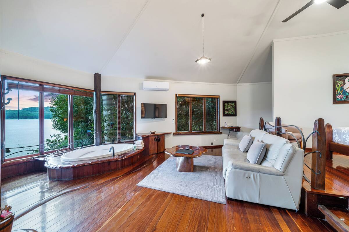 A spacious living room with a large window, a sofa, a coffee table, and a wooden floor.