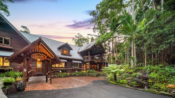 A lodge with a wooden facade, a welcoming entrance, and a paved driveway. - Secrets on the Lake (North Maleny)