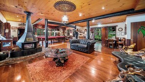 A spacious living room with a large fireplace, leather sofa, and a dining area with wooden furniture. - Secrets on the Lake (North Maleny)