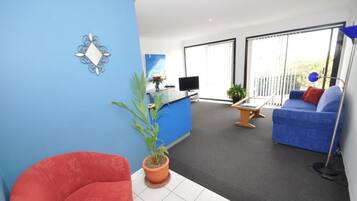 A modern living room with a blue sofa, a red chair, a TV, and a balcony with large windows.