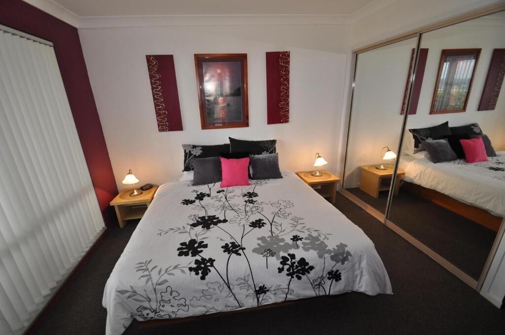 A hotel room with a large bed, two bedside tables with lamps, a mirror, and decorative wall panels.