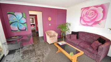 Una sala de estar con un sofá morado, una mesa de centro, una silla y un cuadro de una rosa.