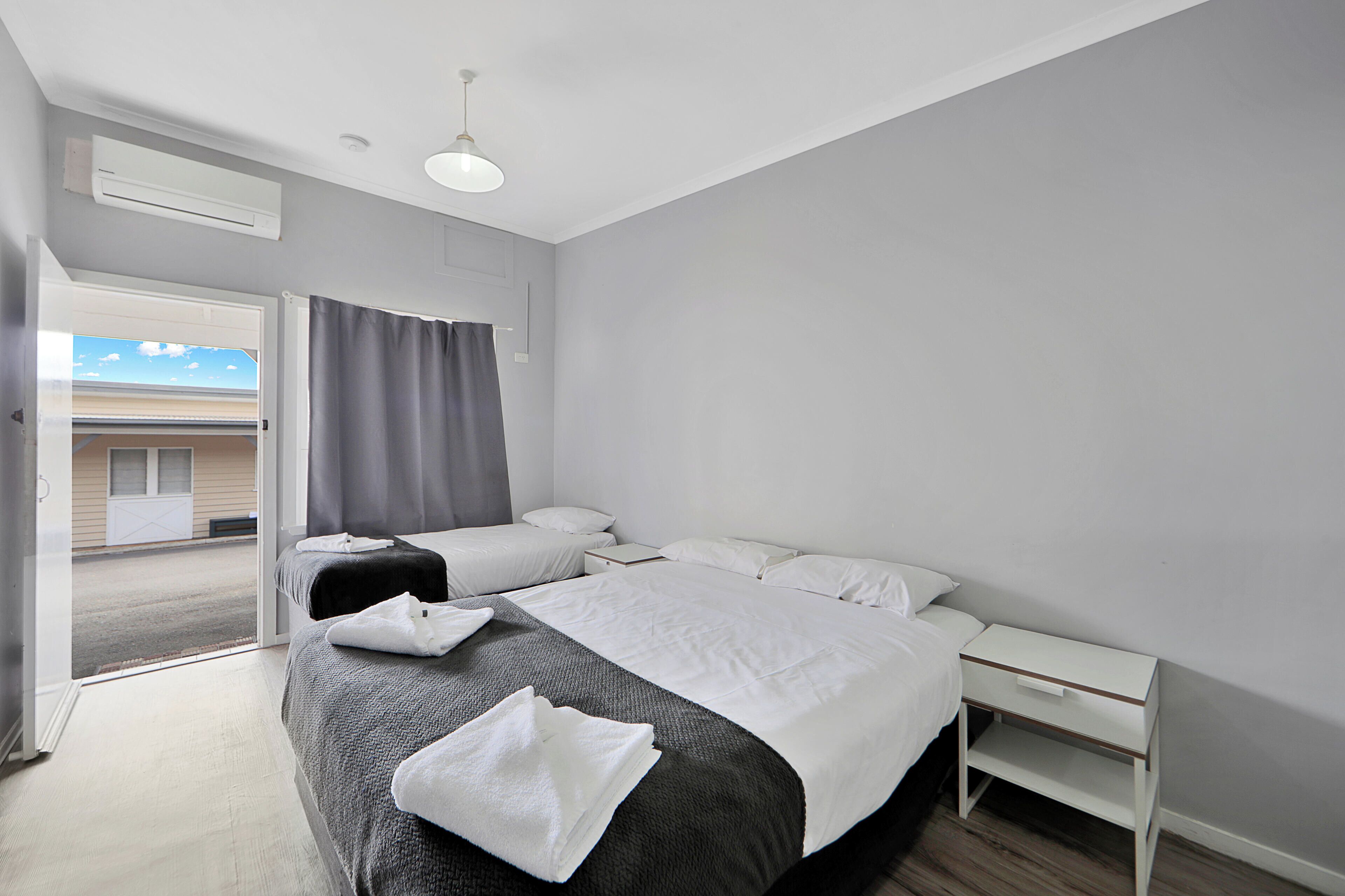 A hotel room with two beds, a white nightstand, and a window with curtains.