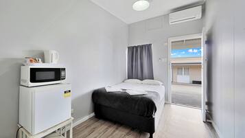 A small, clean room with a bed, a microwave, and a small table.