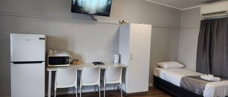 Quarto de hotel compacto com uma cama, escrivaninha com cadeira, micro-ondas, frigorífico, televisão e guarda-roupa.
