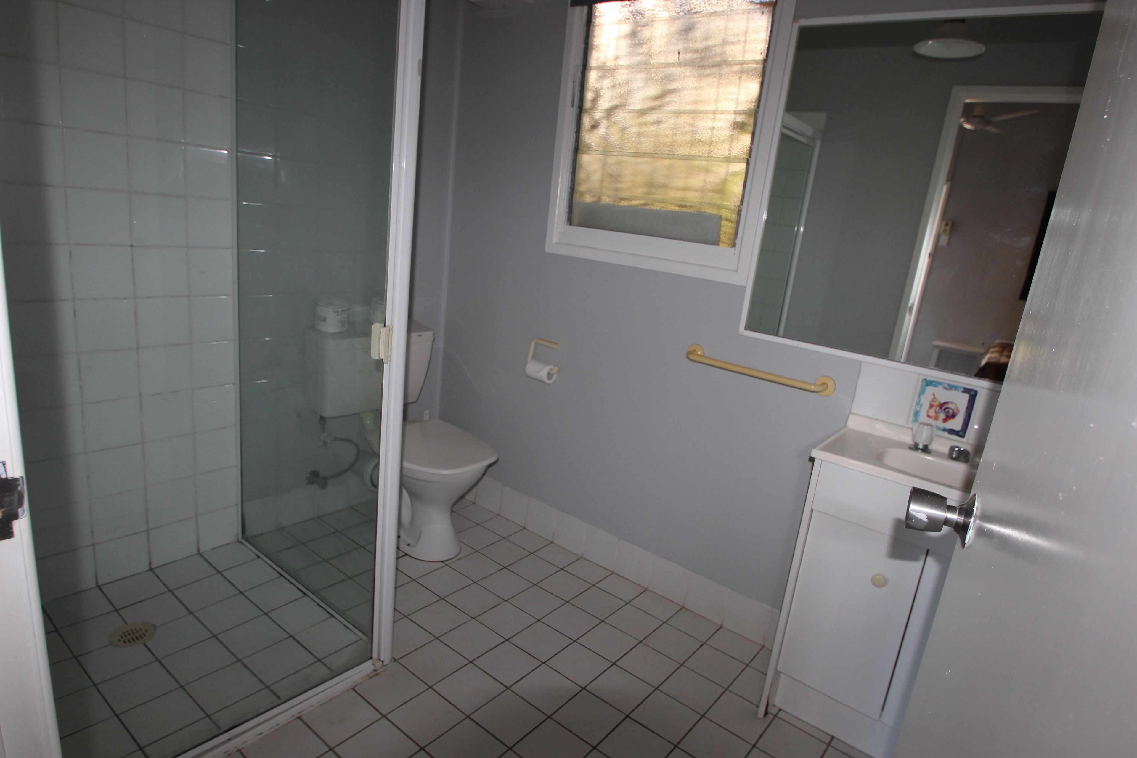 Une salle de bain avec une douche à parois de verre, des toilettes, un lavabo avec un miroir et une fenêtre.