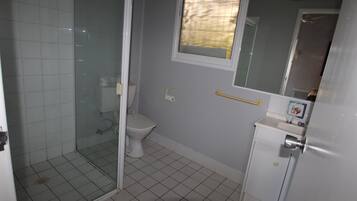 Une salle de bain avec une douche à parois de verre, des toilettes, un lavabo avec un miroir et une fenêtre.