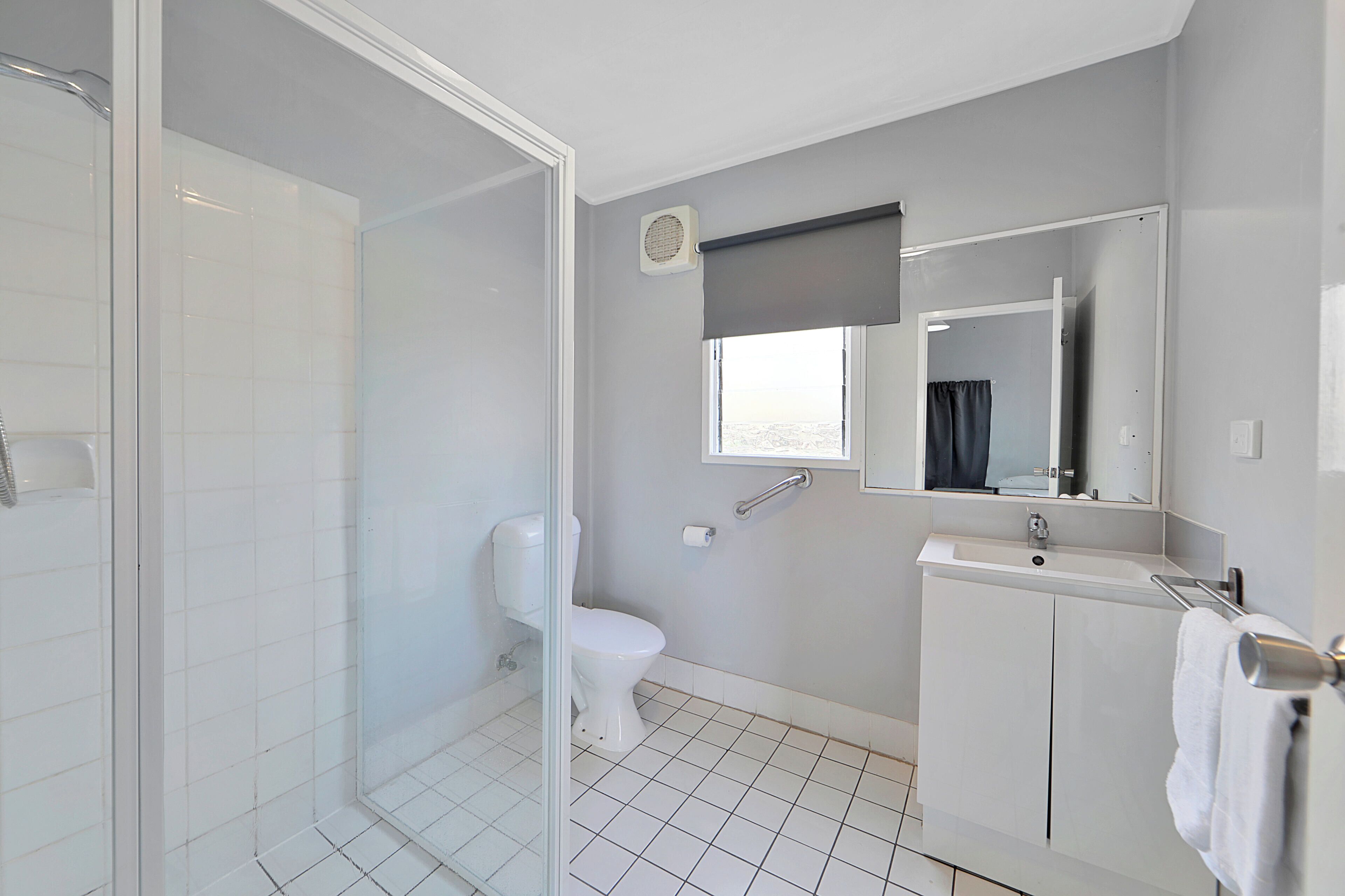 A modern bathroom with a glass shower enclosure, a toilet, a sink with a mirror, and a window with a view.