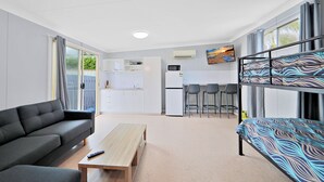 A modern room with a sofa, a wooden table, a bunk bed, a kitchen area, and a dining set. - Ned Kelly's Motel (Tinana)
