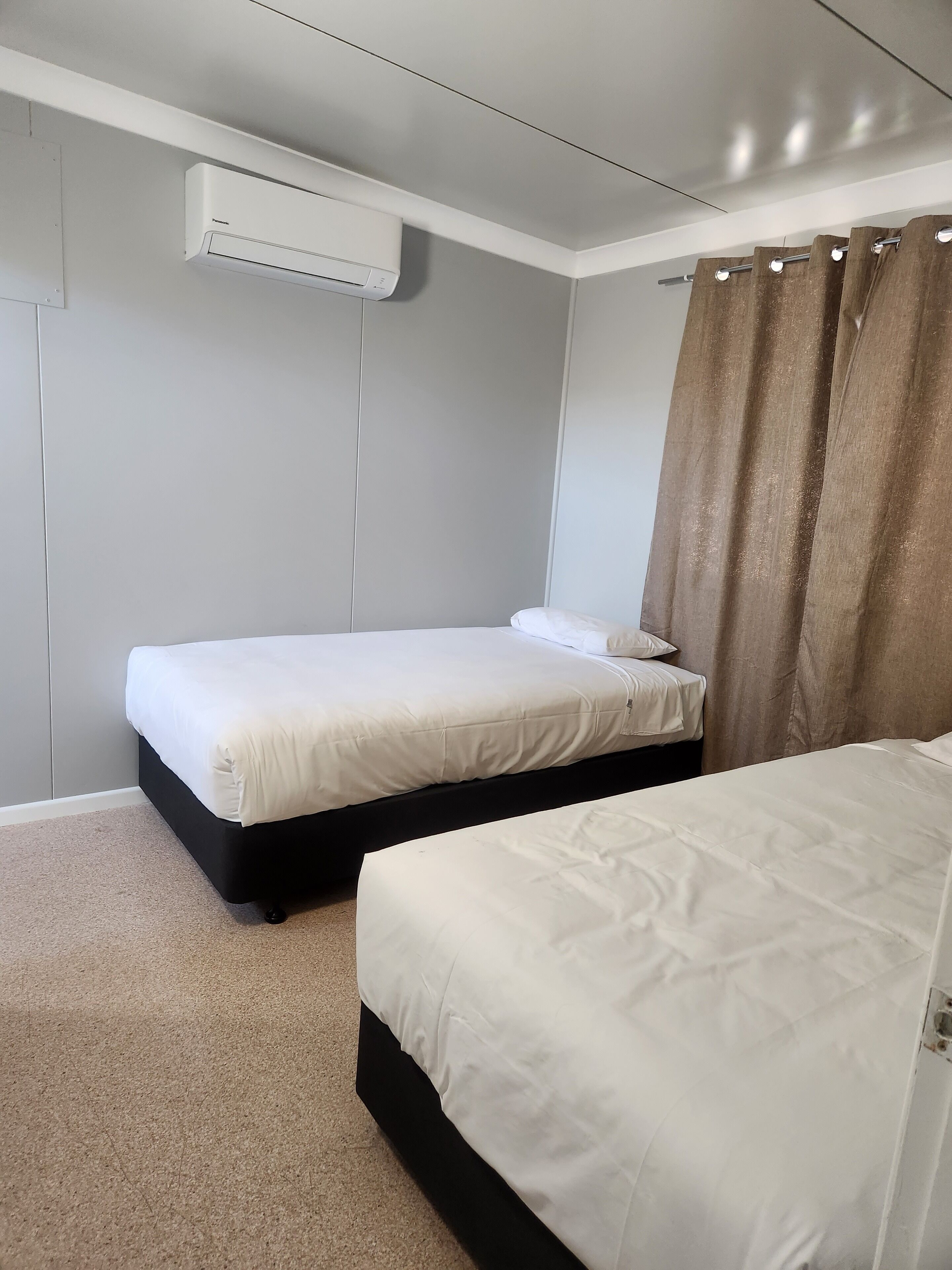 Un dormitorio con dos camas, aire acondicionado en el techo y una cortina.