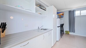 A modern kitchen with white cabinets, a grey countertop, and a built-in microwave. - Ned Kelly's Motel (Tinana)