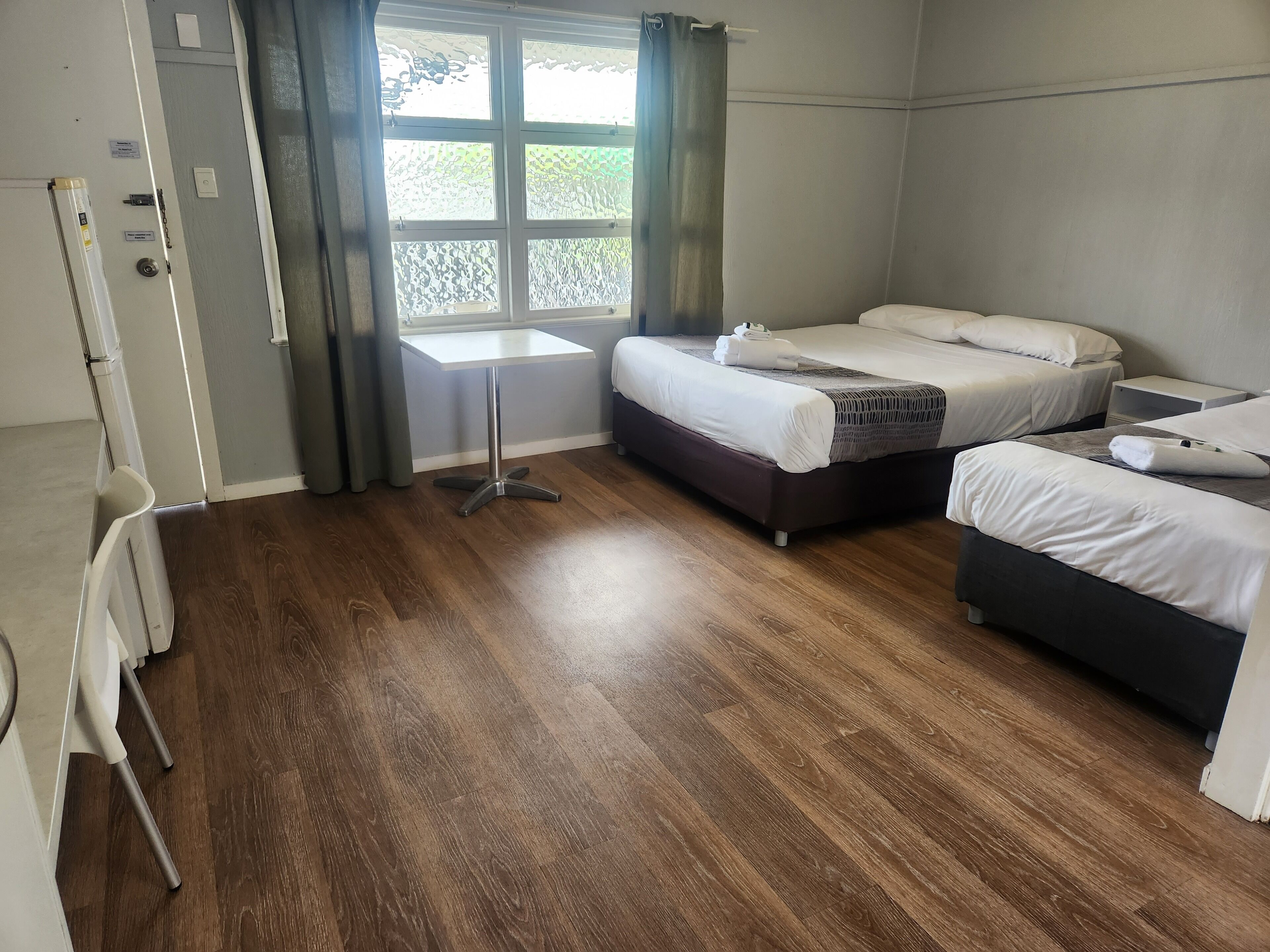 Een hotelkamer met twee bedden, een tafeltje en een raam met gordijnen.