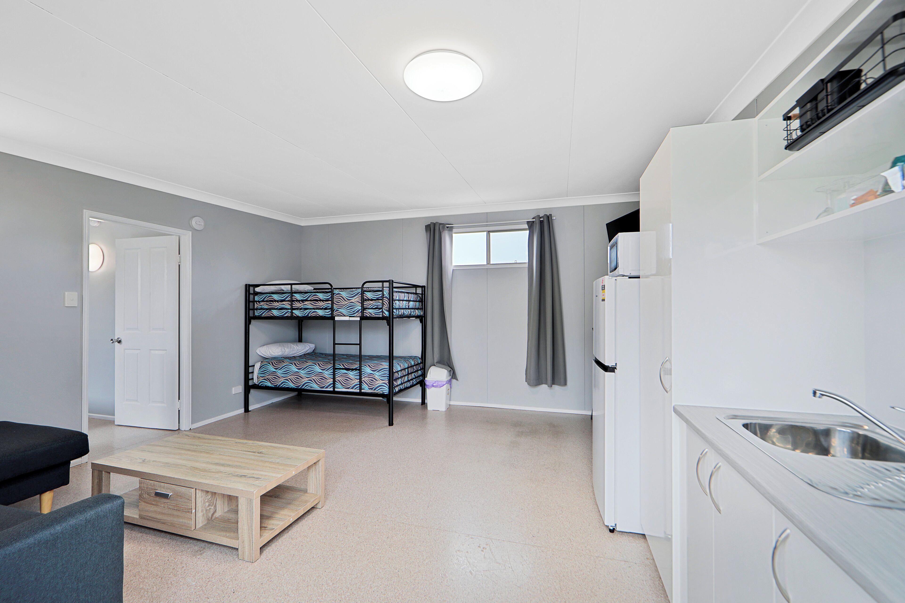 A compact room with bunk beds, a kitchenette, and a small seating area.