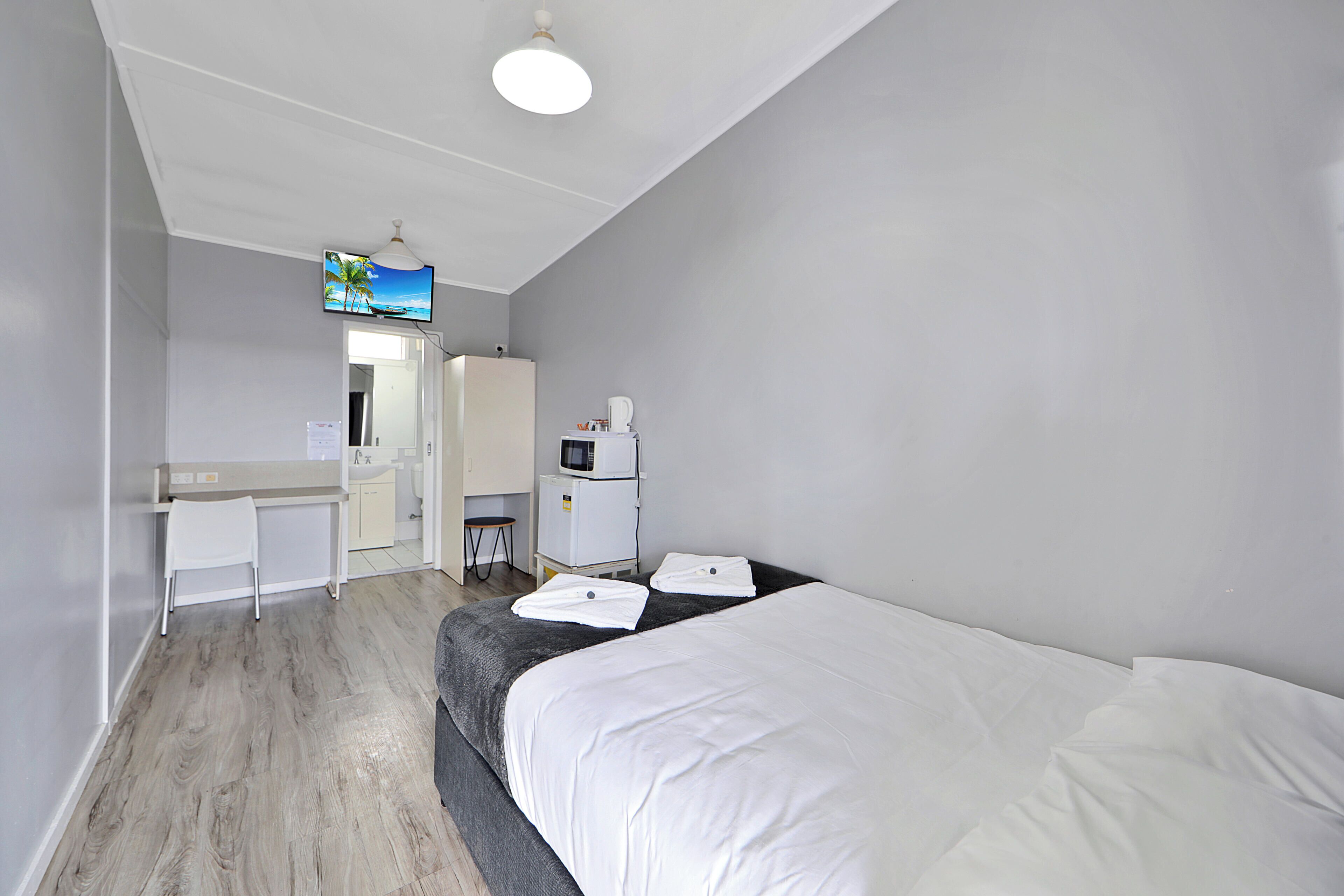 Ein Hotelzimmer mit einem Bett, einem Schreibtisch, einem Sessel, einer Mikrowelle und einem Fernseher an der Wand.