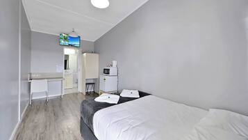 Ein Hotelzimmer mit einem Bett, einem Schreibtisch, einem Sessel, einer Mikrowelle und einem Fernseher an der Wand.