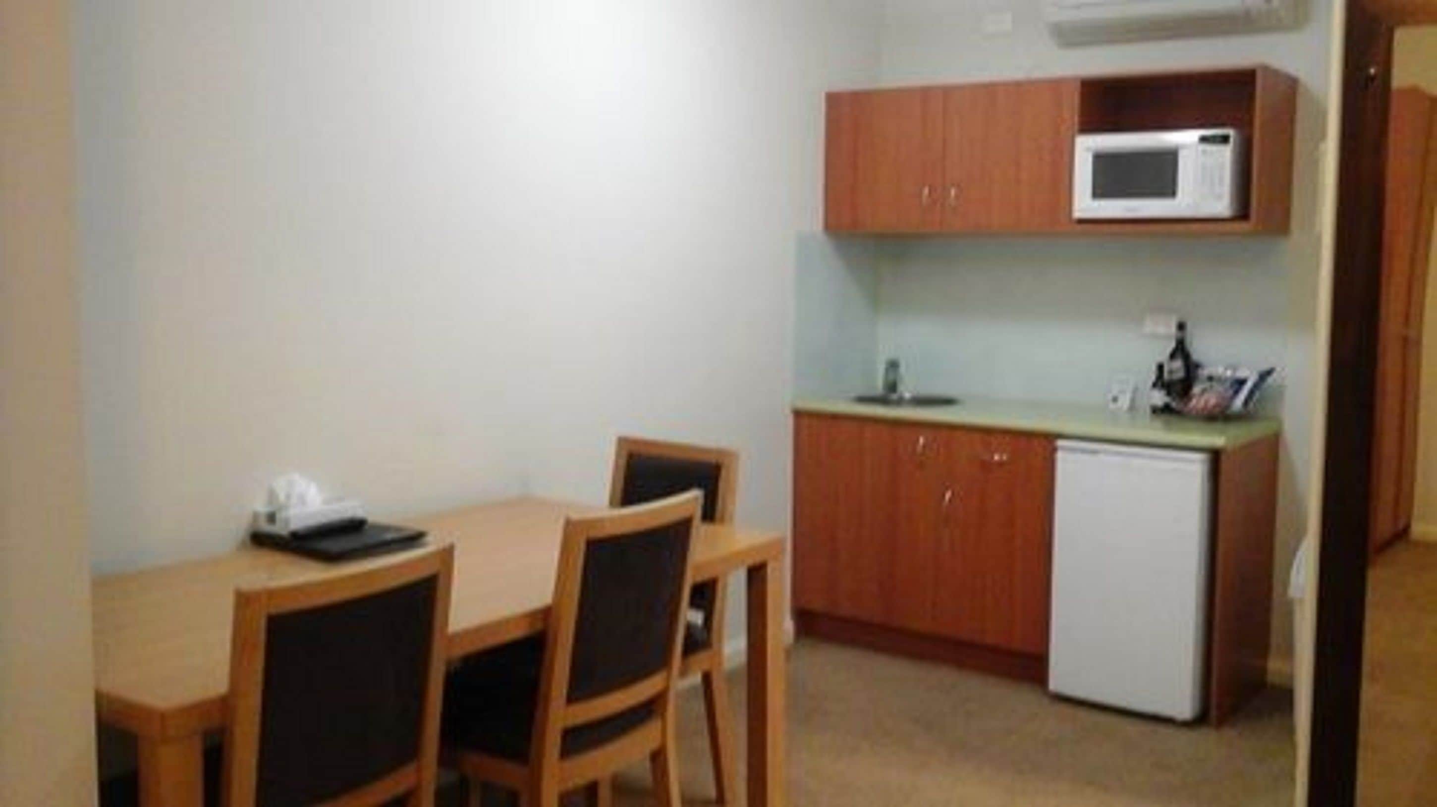 Una pequeña cocina con microondas, lavaplatos y refrigerador. Hay una mesa de madera con dos sillas.