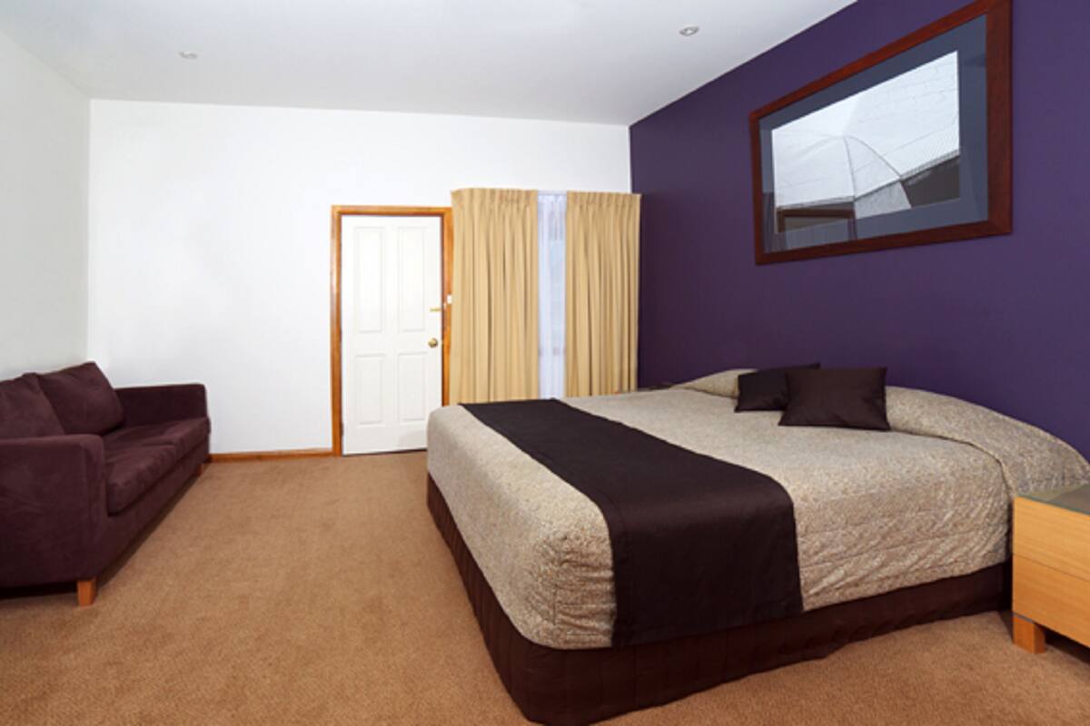 Un dormitorio con cama, sofá, puerta y ventana con cortinas.