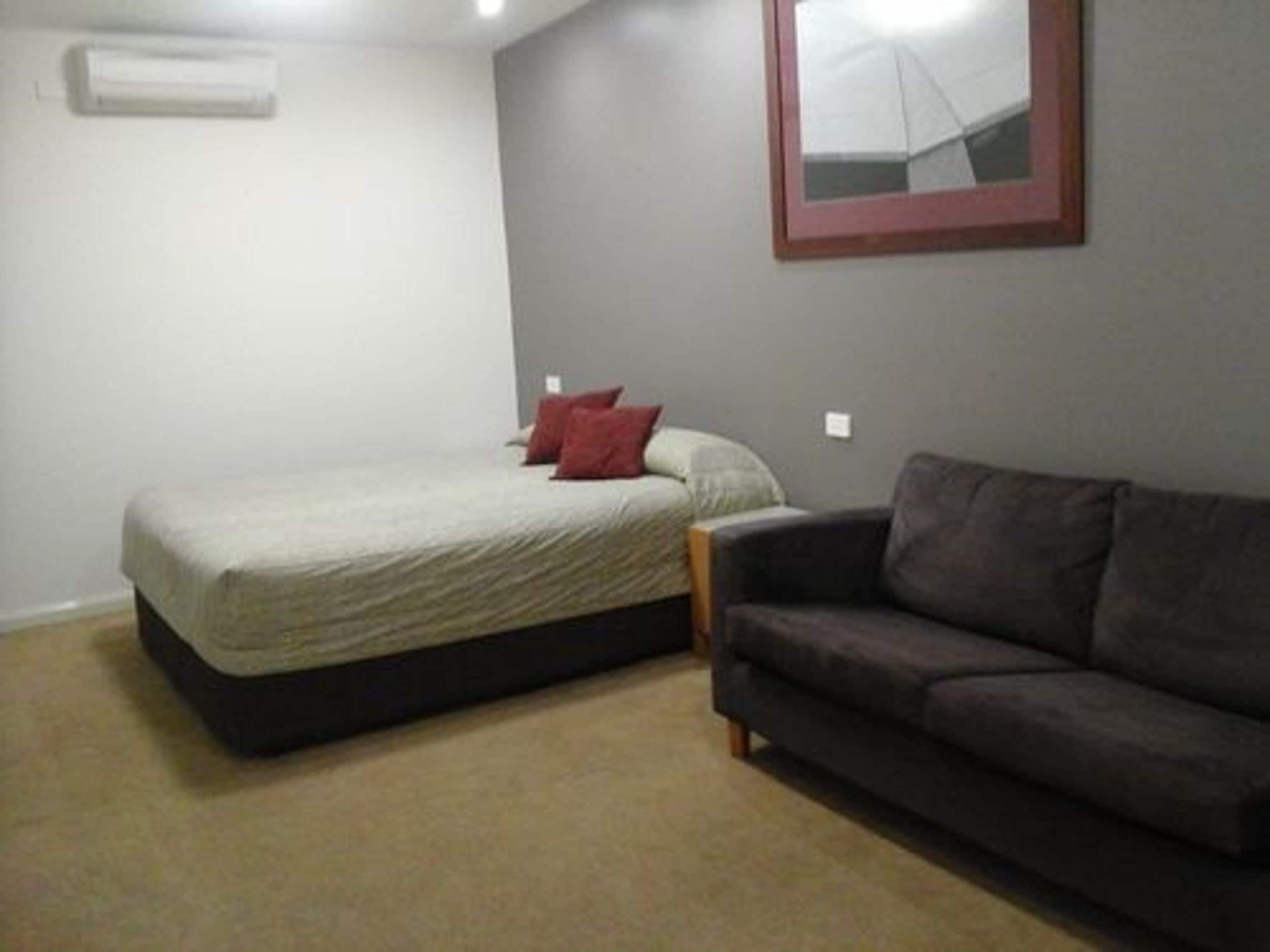 Un dormitorio con una cama, un sofá de color oscuro y un cuadro en la pared.