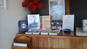 A reception desk with a vase of red flowers, a framed sign, and several brochures. - Willows Motel Goulburn (Goulburn)