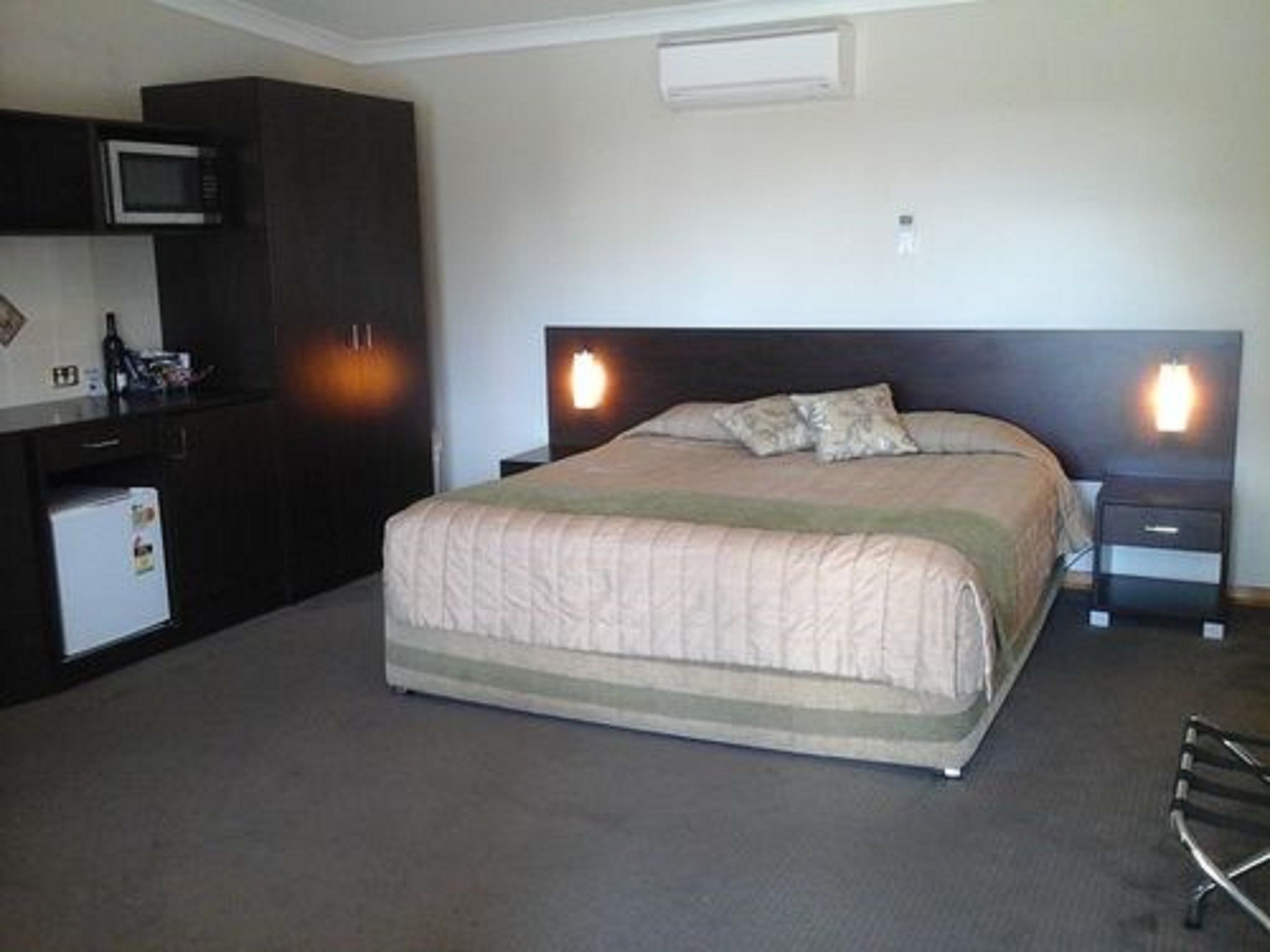 A hotel room with a bed, bedside tables, a small kitchenette with a microwave, and a refrigerator.